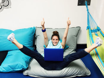Portrait of woman with laptop showing thumbs up sign on mattress at home