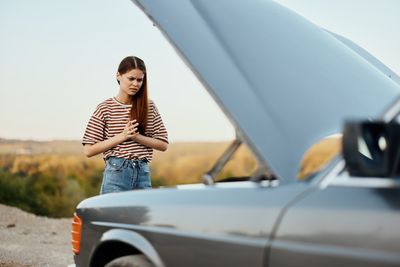 Side view of woman using mobile phone while sitting on car