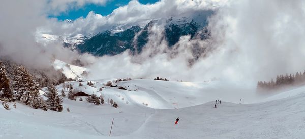 Panoramic view of people skiing on snowcapped mountains against cloudy sky