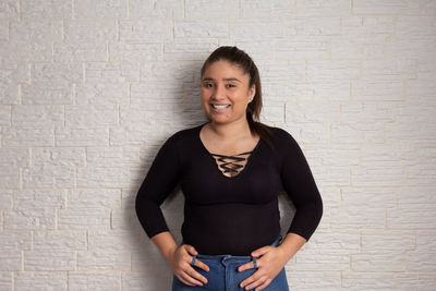 Portrait of smiling young woman standing against wall