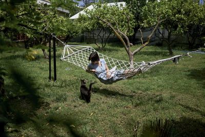 Woman lying on hammock with cat in garden