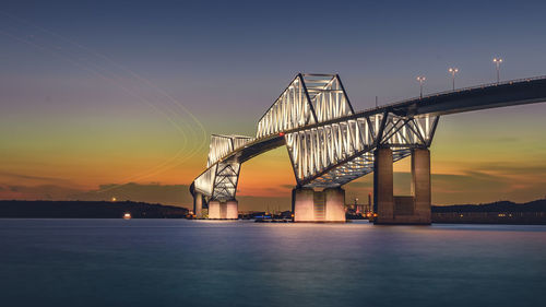 Illuminated bridge over river against sky at sunset