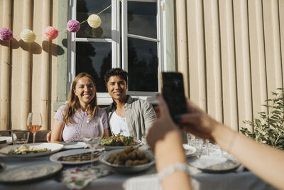 Hand of woman clicking picture of male and female friends during dinner party at cafe