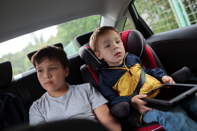Boys using digital tablet while sitting in car