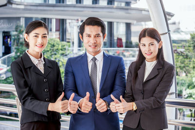 Portrait of smiling colleagues showing thumbs up while standing in office