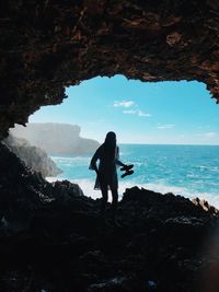 Man standing on rock by sea against sky