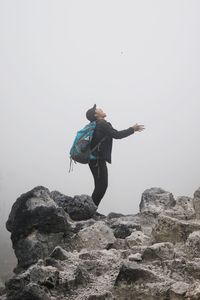 Side view of young man with backpack standing on mountain during foggy weather