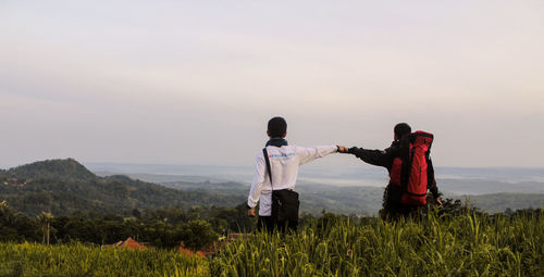 Rear view of couple standing on land against sky during sunset