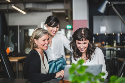 Creative businesswomen smiling while discussing over laptop at desk in office