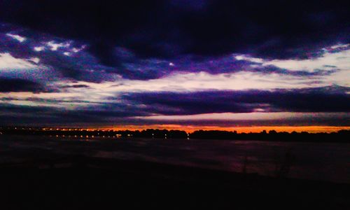 Scenic view of landscape against cloudy sky at sunset