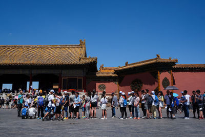 Group of people in front of built structure against blue sky
