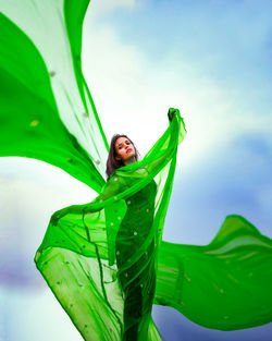 Portrait of young woman with large fabric against sky