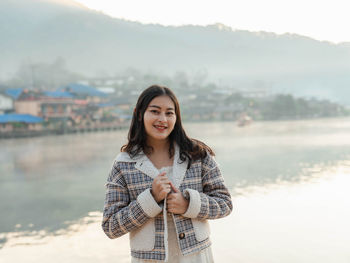 Happy asian woman in winter jacket with fog on the lake view in morning at ban rak thai village