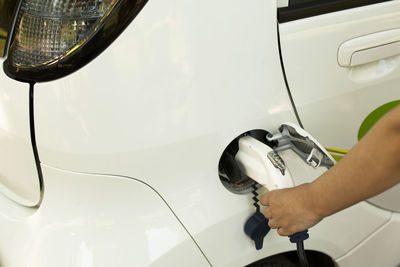 Cropped hand of person charging white electric car