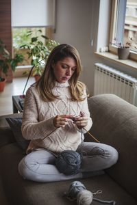 Mid adult woman knitting while sitting on sofa at home