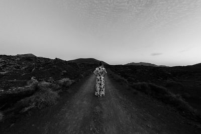 Rear view of man walking on road against clear sky