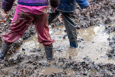 Low section of friends standing in muddy puddle at land