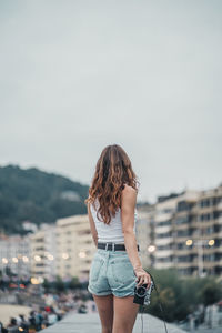 Rear view of woman standing against sky in city