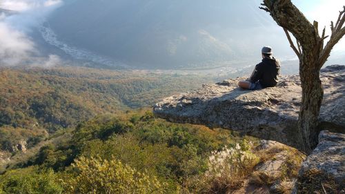 Rear view of man sitting on cliff looking at landscape