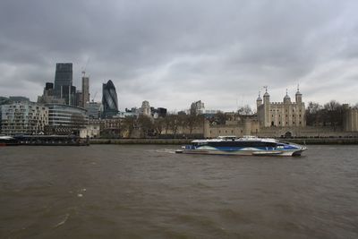 View of buildings by river against cloudy sky