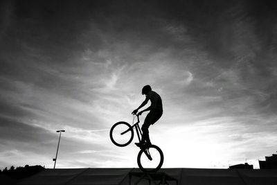 Low angle view of silhouette man with bicycle against sky