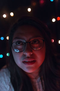 Close-up of young woman against illuminated lights at home