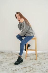 Portrait of young woman sitting on seat against wall