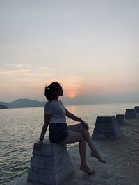 Rear view of girl sitting on beach during sunset