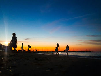 Silhouette people on beach against sky during sunset