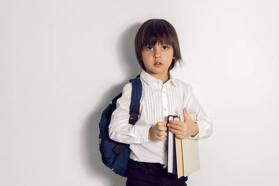 Child boy with a book textbook and backpack stands on a white background