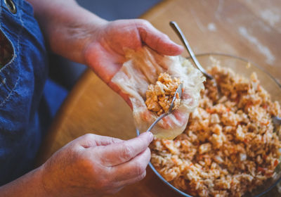 The hands of a senior woman hold a raw leaf of sauerkraut and put a metal teaspoon of rice-meat