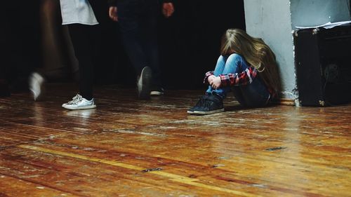 Low section of people walking by sad girl sitting on floor