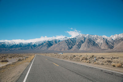 Road by snowcapped mountains against clear blue sky