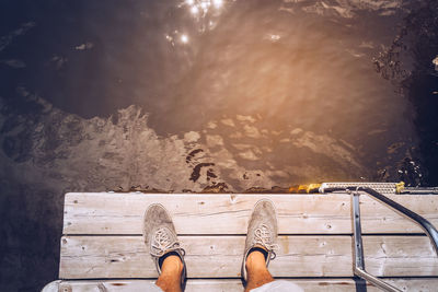 Low section of man standing on boardwalk over lake