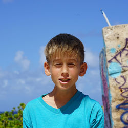 Close-up of boy making face against sky