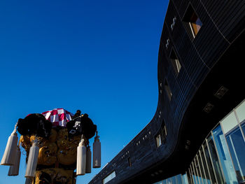 Low angle view of sculpture against building against clear blue sky