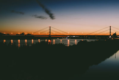 Silhouette of suspension bridge over river during sunset