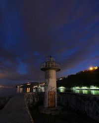 Lighthouse by sea against cloudy sky