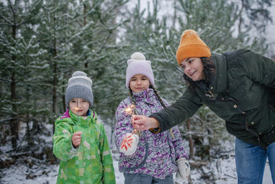 Cheerful mother and kids holding sparkler during winter