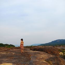 Rear view of woman standing by mountain against sky