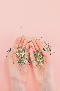 Cropped hands of woman holding confetti against pink background