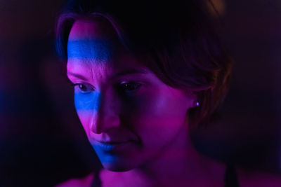 Stripes of blue and purple neon light up the face of a young dark-haired woman