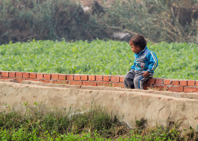 Boy looking away while sitting on retaining wall