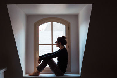 Side view of woman sitting at window