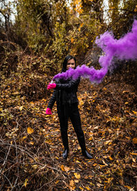 Young woman holding distress flare while standing in forest during autumn