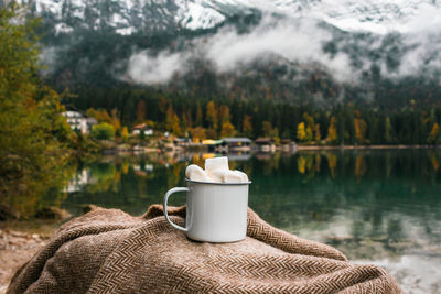 Picnic in bavarian mountains, germany. hand with mug of cacao and marshmallow on the lake background