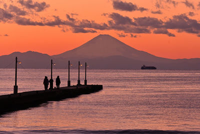Silhouette people on sea by mountains against sky during sunset