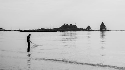 Fisherman fishing in sea against sky