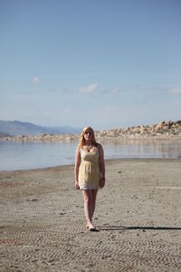 Full length of young woman walking at beach against sky