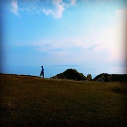 Woman standing on landscape against cloudy sky